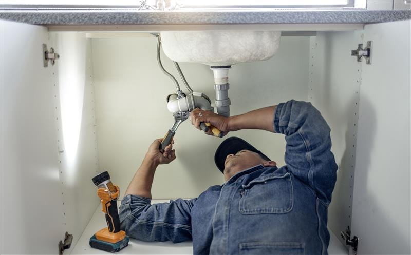Plumber repairing pipes beneath a bathroom sink in Ruskin