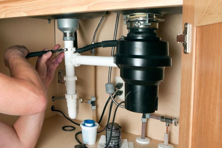 Plumber installing a garbage disposal beneath a kitchen sink in Ruskin