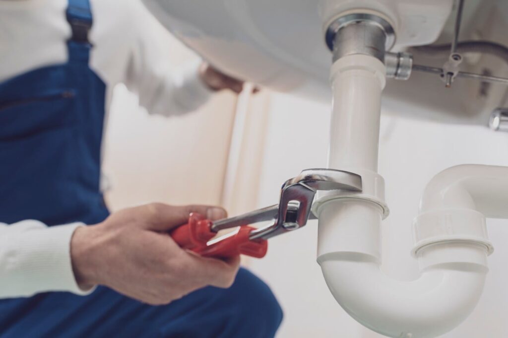 Plumber repairing a white drain pipe beneath a sink in Ruskin